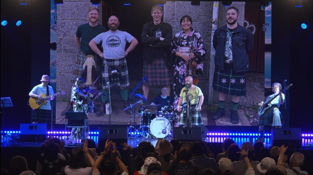 Rock musicians in front of an audience with their own image projected on a screen behind
