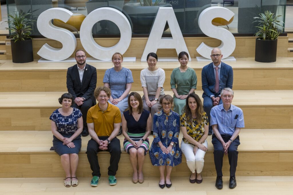 Eleven people seated in front of a large sign reading 'SOAS'